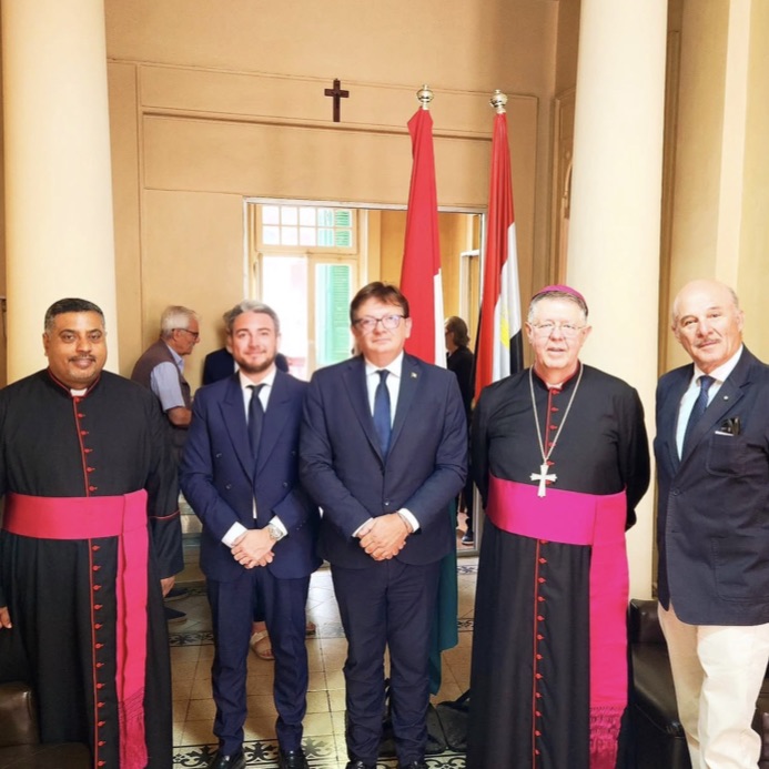 Enrico Celiberti in gruppo con due religiosi e due ospiti, tra le bandiere in una sala